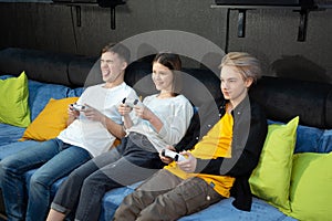 Group of friends of teenagers, boys and girls playing video games on a console in a game club.