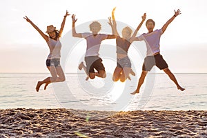 Group of friends together on the beach having fun. Happy young people jumping on the beach. Group of friends enjoying