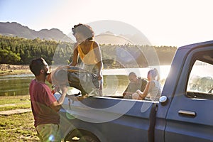 Group Of Friends Unloading Backpack From Pick Up Truck On Road Trip By Lake In Countryside