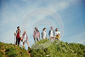 Group of friends walking in meadow on warm, sunny, summer day. Young people standing on hill and enjoying nature