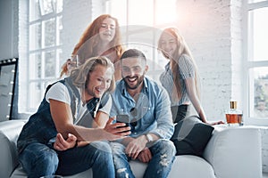 Group of friends watching something funny in the smartphone showing by blonde haired man