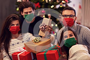 Group of friends wearing masks exchanging Christmas presents at home
