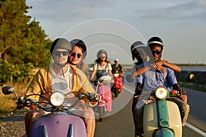 Group of friends wearing protective helmets while riding vintage moto scooters together outside the city