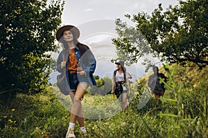 Group of friends, young men and women walking, strolling together outskirts of city, in summer forest, meadow. Active