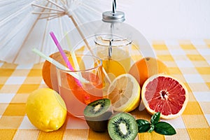 Group of fruits rich in vitamins. Citrus fruits and kiwi. Fruit juice. Yellow checkered tablecloth and white umbrella. Healthy