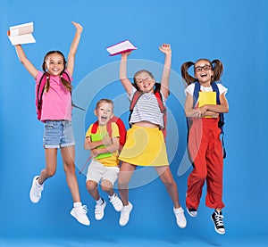 Group of funny excited classmates girls and boy with backpacks and copybooks jumping up in air