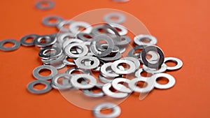 A group of galvanized metal washers falling on a vivid orange color background in slow motion.