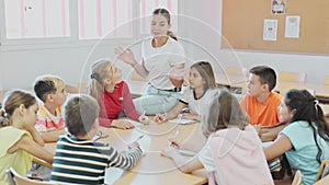 Group of girls and boys studying in school, sitting around desks and attending teacher's lecture.