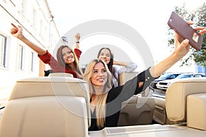 Group of girls having fun in the car and taking selfies with camera.