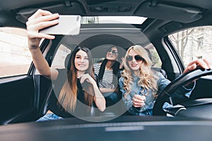 Group of girls having fun in the car and taking selfies with camera