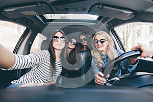 Group of girls having fun in the car and taking selfies with camera on road trip