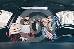 Group of girls having fun in the car and taking selfies with camera on road trip