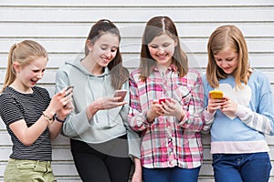 Group Of Young Girls Outdoors Looking At Messages On Mobile Phones