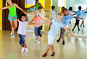 Group of children practicing vigorous jive movements in dance class with female coach photo