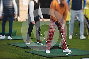 Group of golfers practicing and training golf swing on driving range practice, men playing on golf course, golf ball at golfing