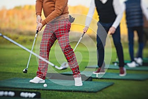 Group of golfers practicing and training golf swing on driving range practice, men playing on golf course, golf ball at golfing