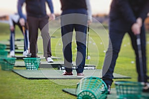 Group of golfers practicing and training golf swing on driving range practice, men playing on golf course, golf ball at golfing