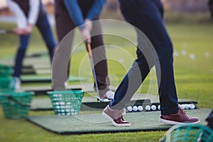 Group of golfers practicing and training golf swing on driving range practice, men playing on golf course, golf ball at golfing