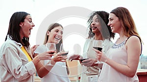 A group of gossip females talking and laughing holding a wine glasses at home party. Young adult women friends bonding