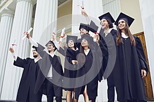 A group of graduate students raised their hands with diplomas up