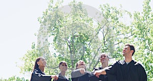 Group of graduates celebrating and throwing caps or hats into the air in tradition after university campus graduation