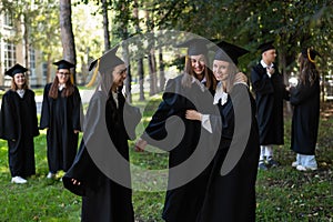 A group of graduates in robes congratulate each other on their graduation outdoors.