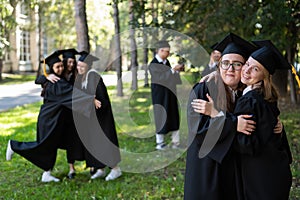 A group of graduates in robes congratulate each other on their graduation outdoors.