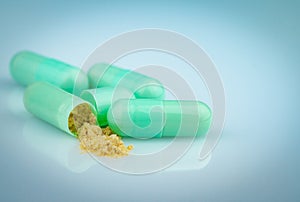 Group of green capsule and open one capsule to show yellow powder of herbal medicine on gradient background. Pharmaceutical