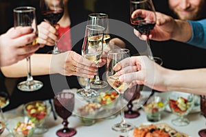 Group of guests celebrate and raise glasses, toasting and cheering with alcohol glasses with wine and champagne in the restaurant