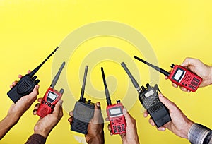 Group of hands holding portable two way radios with yellow background