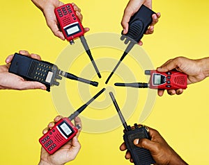 Group of hands holding portable two way radios with yellow background photo