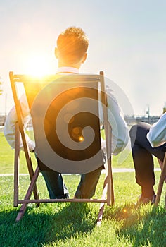 Group of handsome businessmen relaxing and talking about life while sitting on folding chair at park