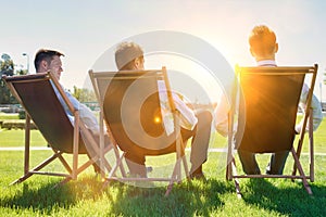 Group of handsome businessmen relaxing and talking about life while sitting on folding chair at park