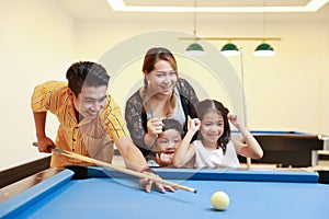 Group of happiness asian family father, mother, son and daughter playing billiard or snooker on blue pool table with happy smiling
