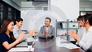 Group of happy Asian business people discuss together in team brainstorm meeting and clap hand, work late night in office