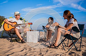 Group of happy Asian friends playing guitar and singing with clapping together having fun and enjoying while camping picnic on the