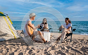 Group of happy Asian friends playing guitar and singing with clapping together having fun and enjoying while camping picnic on the