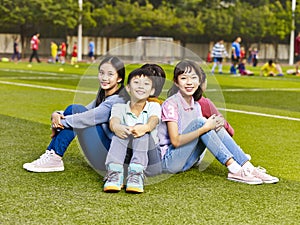 Group of happy asian primary school student sitting on grass on