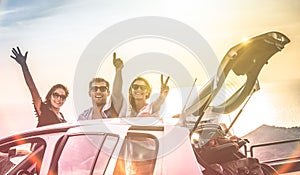 Group of happy best friends cheering on car road trip at sunset