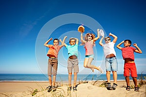 Group of happy boys and girls jump on sand beach