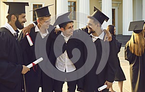 Group of happy boys students university graduates mates standing and hugging with diplomas in hands