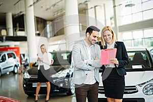 Group of happy car sales consultants working inside vehicle showroom