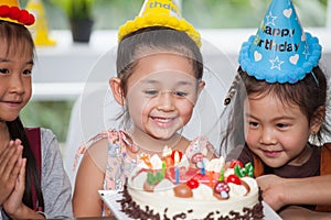 group of happy children girl with hat blowing candles on  birthday cake together celebrating in party . adorable kids gathered