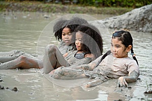Group of happy children girl playing in wet mud puddle on summer day in rainy season