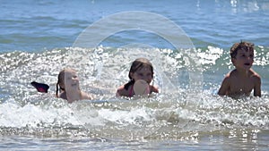 Group of happy children are laying in splashing sea waves on the beach