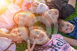 A group of happy children are lying in the park on the green grass and smiling. The concept of summer and happy childhood.