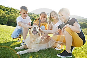 Group of happy children playing on green grass in a spring park with a dog.