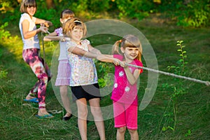 Group of happy children playing tug of war outside on grass