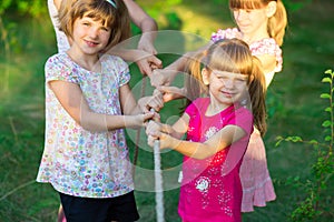 Group of happy children playing tug of war outside on grass