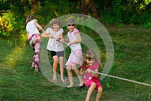 Group of happy children playing tug of war outside on grass